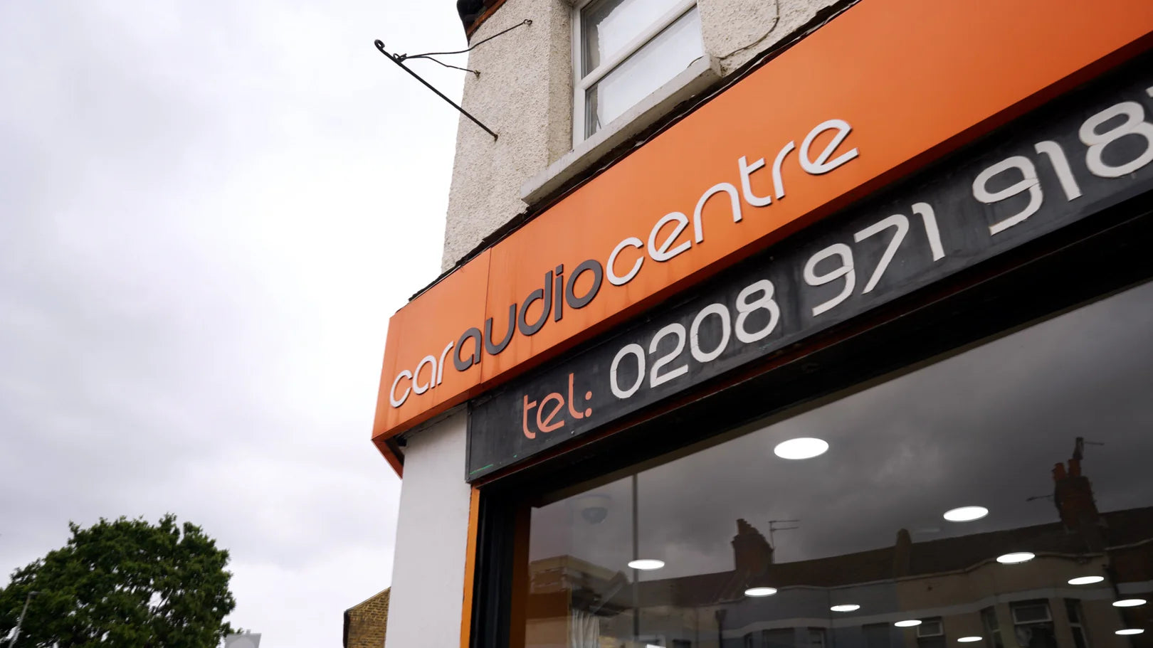 Car audio centre storefront with contact information on an orange sign.