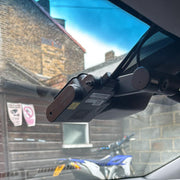 A black car dash cam mounted on a windshield bracket inside a vehicle, with a brick building and a blue motorcycle visible through the window.