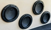 Four black circular car subwoofers mounted on a beige wall.